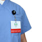 Close-up of a person wearing a light blue scrub top with a badge labeled "Clear PHYSICIAN Badge Buddy - Horizontal ID Badge Backer for Physicians - Double Sided Print" clipped to the chest pocket, featuring a Red Color Border.