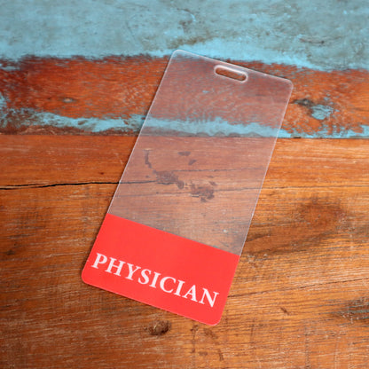 A Clear PHYSICIAN Badge Buddy Vertical with Red Border for Physicians sits on a rustic wooden surface. Sold by Specialist ID.