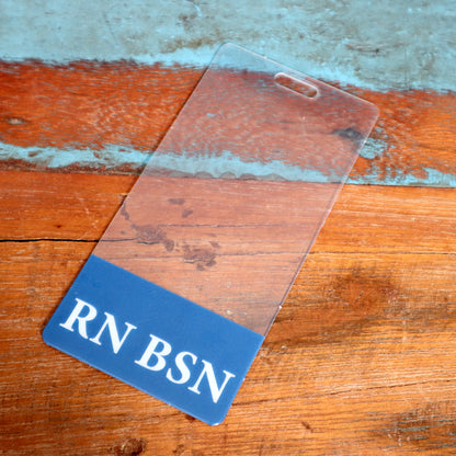A Clear RN BSN Badge Buddy Vertical with Blue Border for Nurses, placed on a wooden surface, is perfect for registered nurses' identification. Sold by Specialist ID.