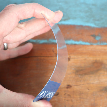 A hand holds a curved, transparent piece of plastic or glass above a wooden surface, demonstrating its flexibility, much like Clear RN BSN Badge Buddy Vertical with Blue Border for Nurses often used by registered nurses for easy identification.