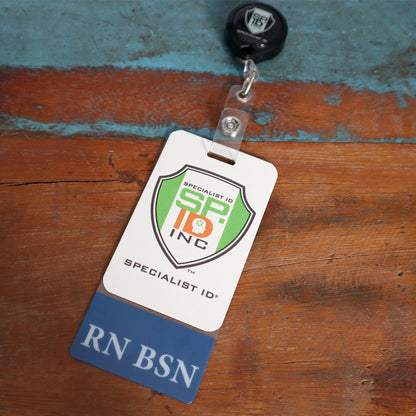 An ID card on a retractable badge reel, featuring the Specialist ID Inc. logo and marked with "RN BSN" on a blue strip at the bottom, rests on a wooden surface, showcasing the Clear RN BSN Badge Buddy Vertical with Blue Border for Nurses ideal for registered nurses' identification needs.