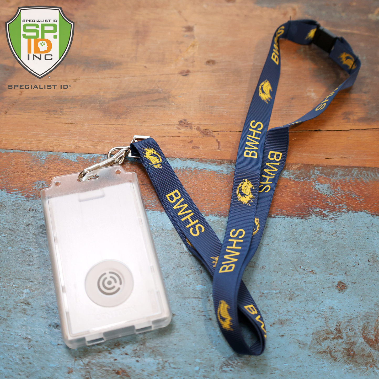 A blue BWHS lanyard with yellow text and logo holds a Dual Badge Holder Compatible with Centegix™ V2 Alarm Card + Standard ID Card, resting on wood. The Specialist ID logo appears in the top left corner.