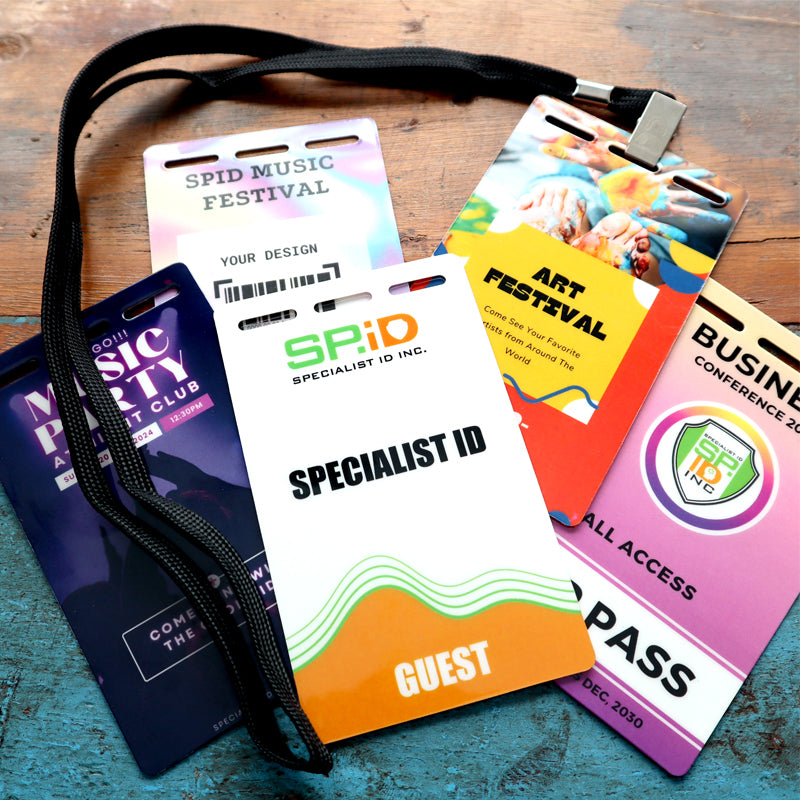 A black lanyard holds several Custom Printed Event Badges with Three Slot Holes— Design It Your Way!—featuring colorful labels for music, art, business, and guest identification on a wooden surface.