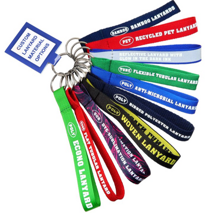 A keyring showcases eight colorful sample lanyards, each labeled with material types such as bamboo, PET, polyester, tubular, woven, and antimicrobial, along with a tag that reads “Custom Printed Lanyards Material Options.” Ideal for selecting your next personalized Custom Printed Lanyard or custom breakaway lanyard.