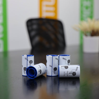 Six small, cylindrical containers with blue rims and illustrated labels—specifically 569946-002 Entrust (Datacard) Adhesive Cleaning Sleeves (5-Pack) for printhead protection—are neatly arranged on a dark table; a blurred chair and colorful wall panels are in the background.