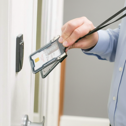 A person in a dress shirt holds an ID card near an access control reader mounted on a wall, likely to gain entry through a secured door using their Identity Stronghold RFID Blocking Secure Badgeholder Classic - Holds 1 Card - Shields 13.56MHz Signal (IDSH1004-001B-002).