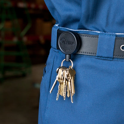 A set of keys attached to a Key-Bak Mid Size Key Ring Badge Reel with Belt Clip (#6) clipped to the belt of a person wearing blue work pants.