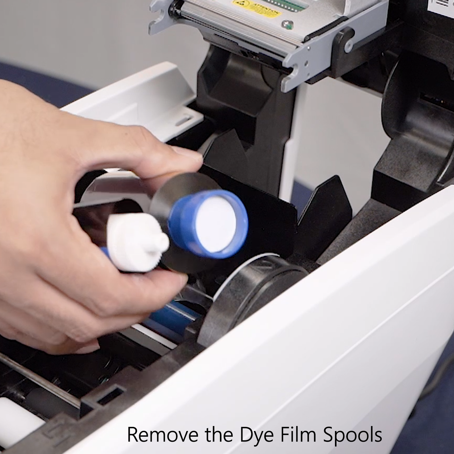 Person removing dye film spools from a printer with text 'Remove the Dye Film Spools'.