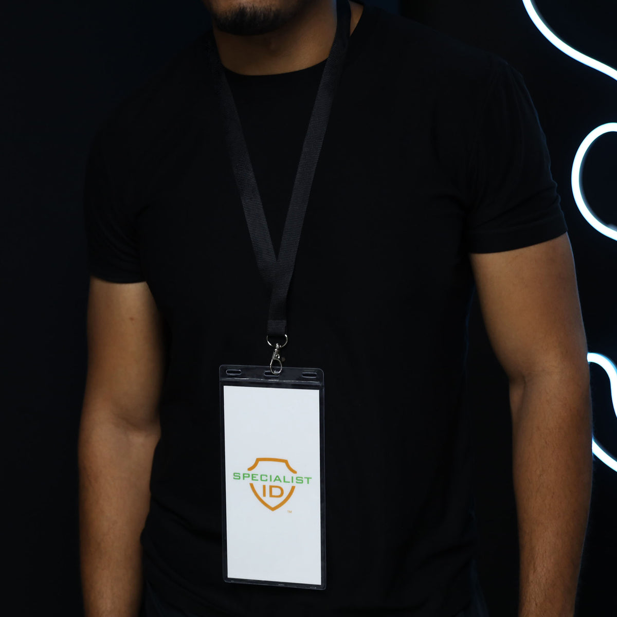 A person wearing a black shirt and a lanyard with a badge that reads “SPECIALIST ID” stands against a dark background, the badge displayed in a 4x8 Inch Clear Vinyl Ticket & Credential Holder with 3 Slots (SPID-1040), ensuring it remains visible and protected.