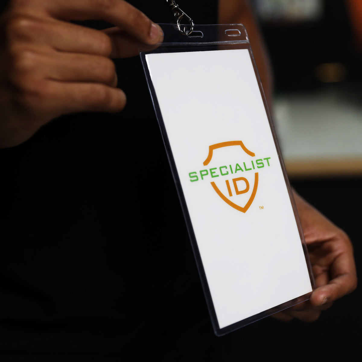 A person holds a 4x8 Inch Clear Vinyl Ticket & Credential Holder with 3 Slots (SPID-1040), displaying a blank white badge featuring the words “SPECIALIST ID” and a green and orange shield logo.