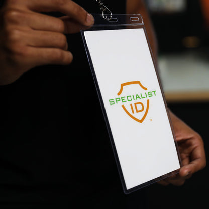 A person holds a 4x8 Inch Clear Vinyl Ticket & Credential Holder with 3 Slots (SPID-1040), displaying a blank white badge featuring the words “SPECIALIST ID” and a green and orange shield logo.