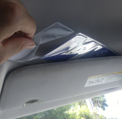 A hand is placing a thin plastic placard into a Specialist ID Handicap Hang Tag Holder (SPID-1120) attached to the underside of a car's sun visor.