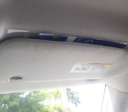 The inside of a car with items such as documents or booklets tucked into the overhead sun visor, complemented by a Specialist ID Handicap Hang Tag Holder (SPID-1120) neatly attached for easy accessibility.