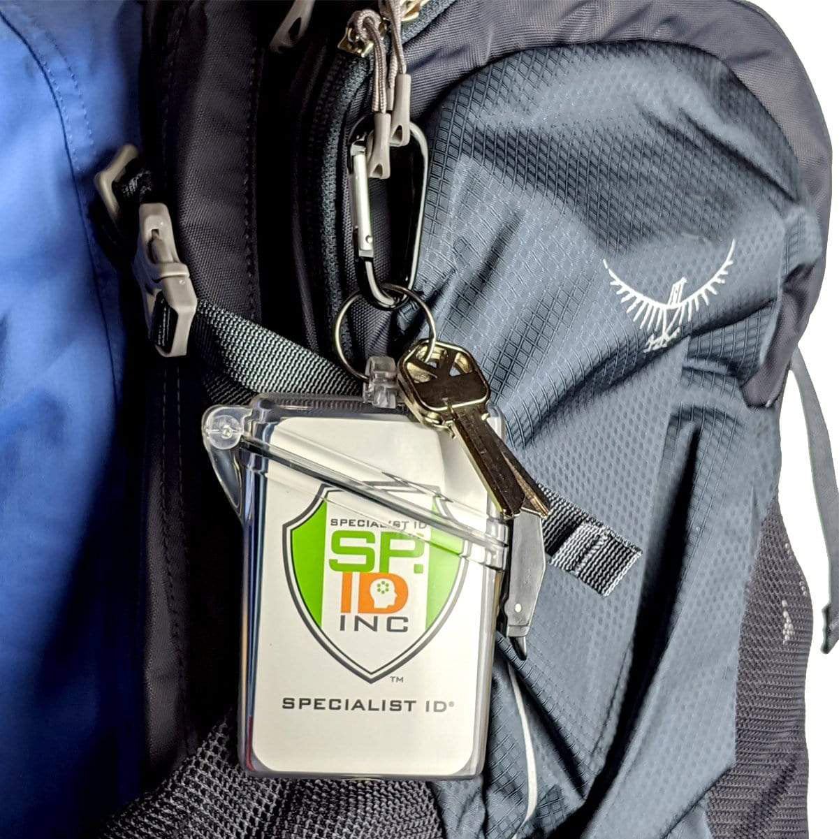 A close-up of a black backpack features a clear Waterproof ID Badge Holder (P/N SPID-1690) with a neck lanyard and a set of keys attached to it. Sold by Specialist ID.