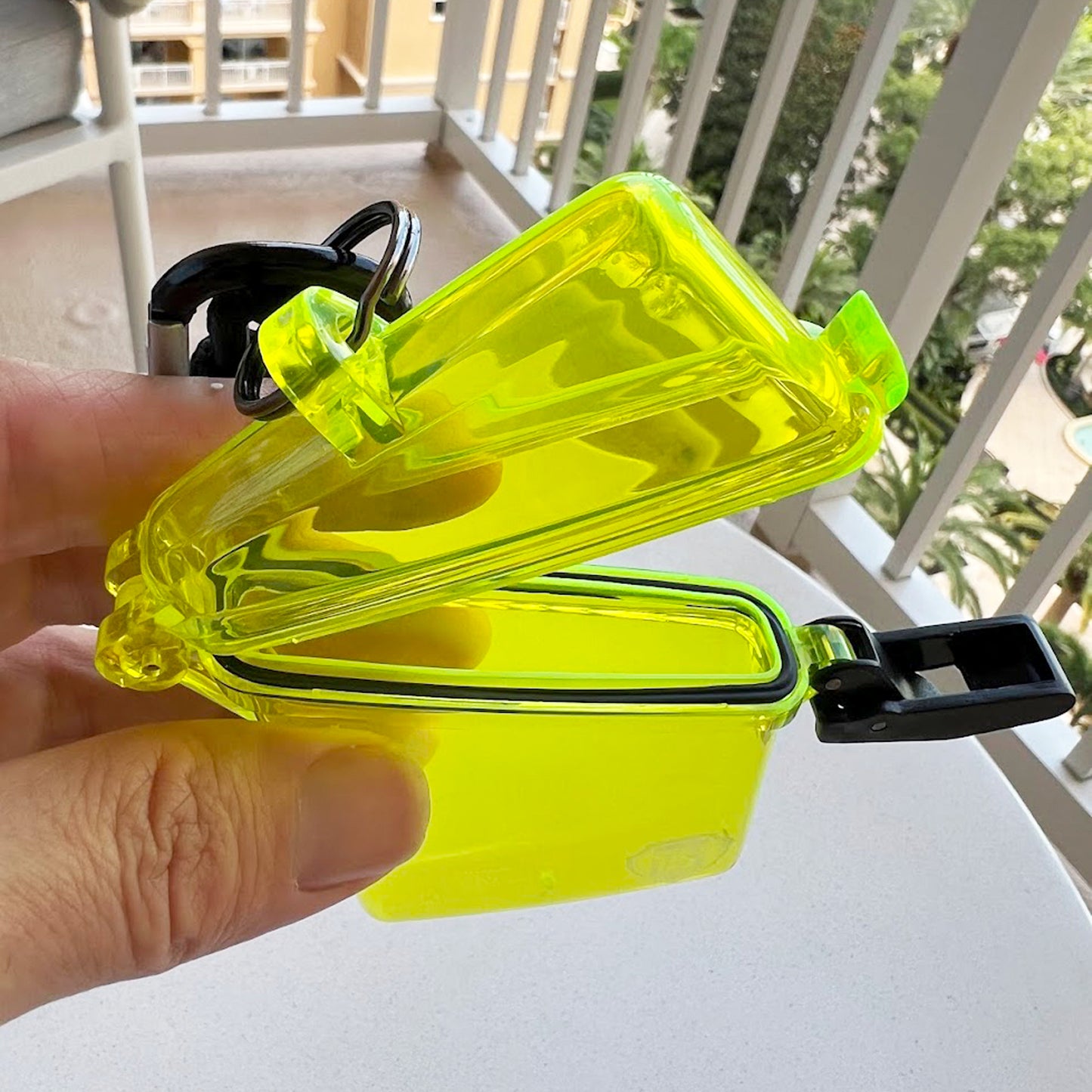 A person stands on a balcony, holding an open, bright translucent yellow Waterproof ID Badge Holder (P/N SPID-1690-YELLOW) made from crush-resistant plastic, featuring a black seal and black clip. Sold by Specialist ID.