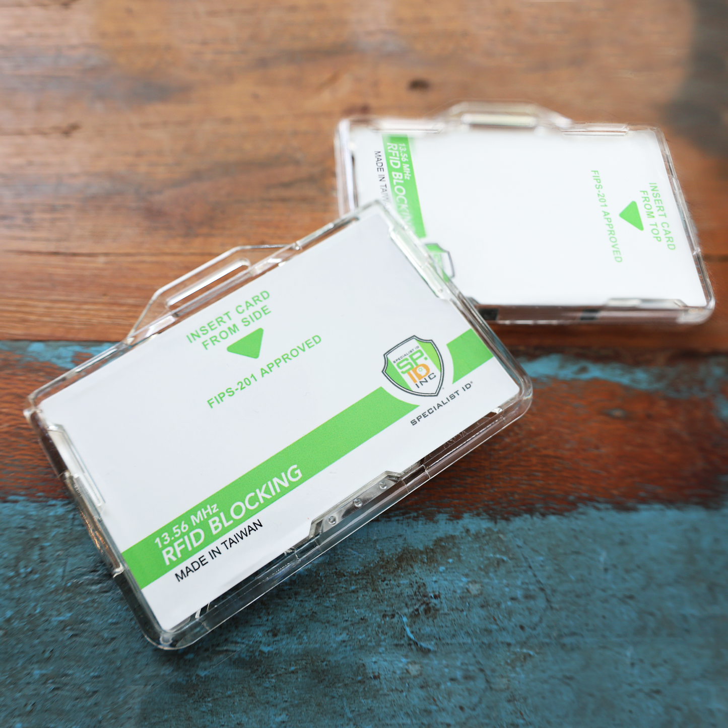 Two Specialist ID Dual Sided RFID Blocking Badge Holders (SPID-1760) shown on a painted wooden surface provide 13.56 MHz RFID protection for CAC, TWIC, PIV, HSPD-12 & secure ID cards.