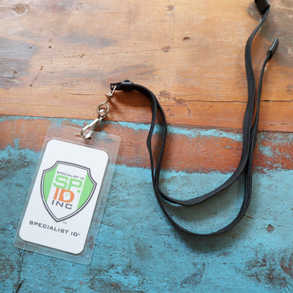 A Short Breakaway Lanyard with Metal Swivel Hook (SPID-2470), designed for students, youth, and smaller frames, displays an ID card with a clear badge holder on a worn blue wooden surface.
