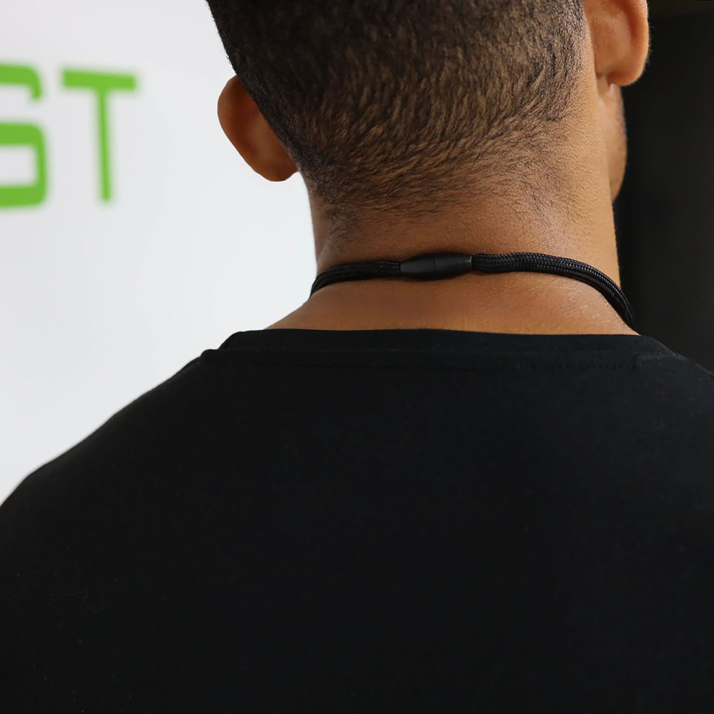 A person is shown from behind wearing a black shirt and a Heavy Duty Breakaway Round Lanyard With Detachable Key Ring (2135-454X), with part of green text visible on a white wall in the background.