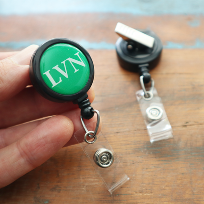 A hand holds the LVN Badge Buddy Reel with Swivel Spring Clip—an all-in-one badge buddy and retractable reel for nurses—while another rests nearby, ideal for Licensed Vocational Nurses needing convenient badge access.