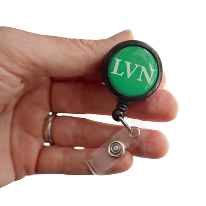 A hand holds the LVN Badge Buddy Reel with Swivel Spring Clip—an all-in-one LVN Badge Buddy and retractable reel for nurses—featuring a green design and clear plastic strap, isolated on a white background.