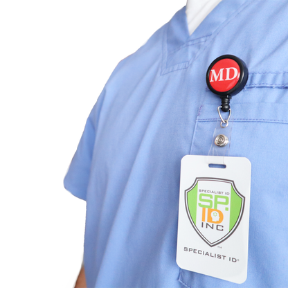 A person wears light blue scrubs with the MD Badge Buddy Reel with Swivel Spring Clip—a combined MD Badge Buddy and retractable reel for doctors—attached to their chest. Sold by Specialist ID.