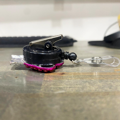 Black and pink Badge Reel with an alligator swivel clip on a wooden surface. Sold by Specialist ID.