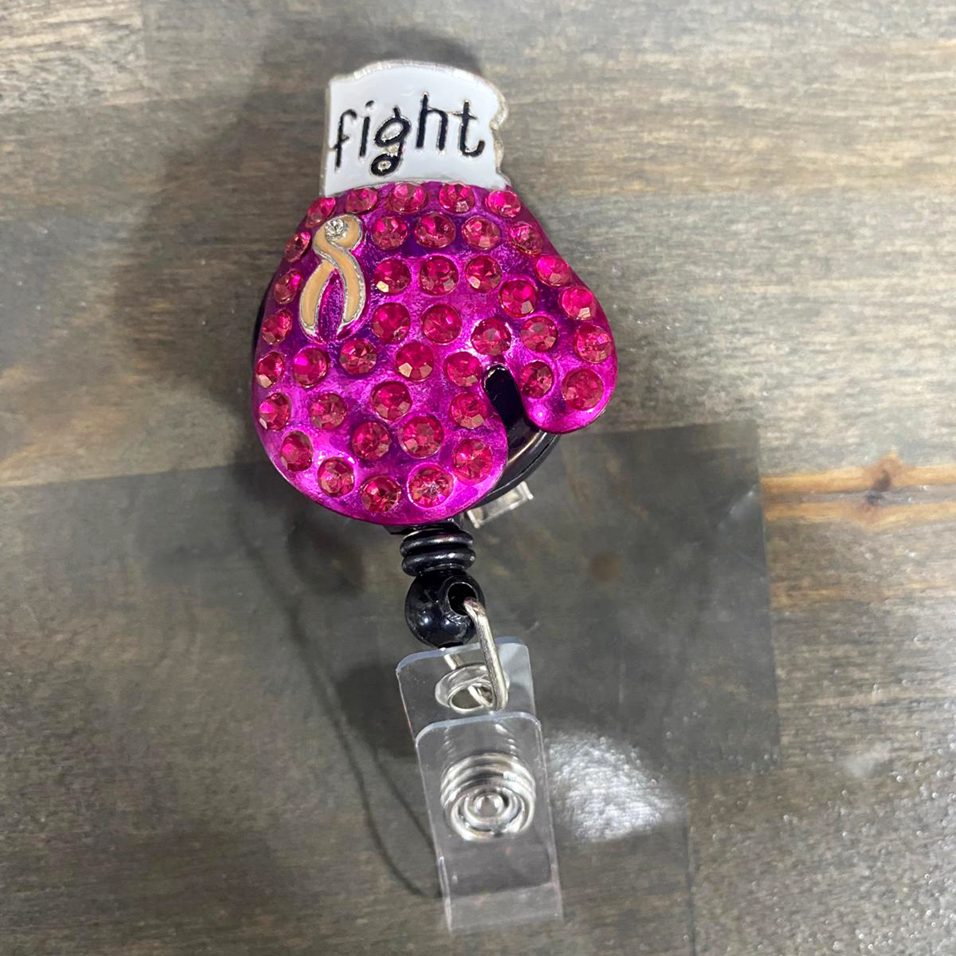 Pink blinged-out boxing glove badge reel with 'fight' text on a wooden surface. Sold by Specialist ID.