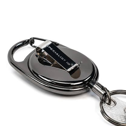A close-up of a polished gunmetal gray retractable keychain badge reel with a clip, featuring the text 'SPECIALIST ID' on the metal clip, set against a plain white background.