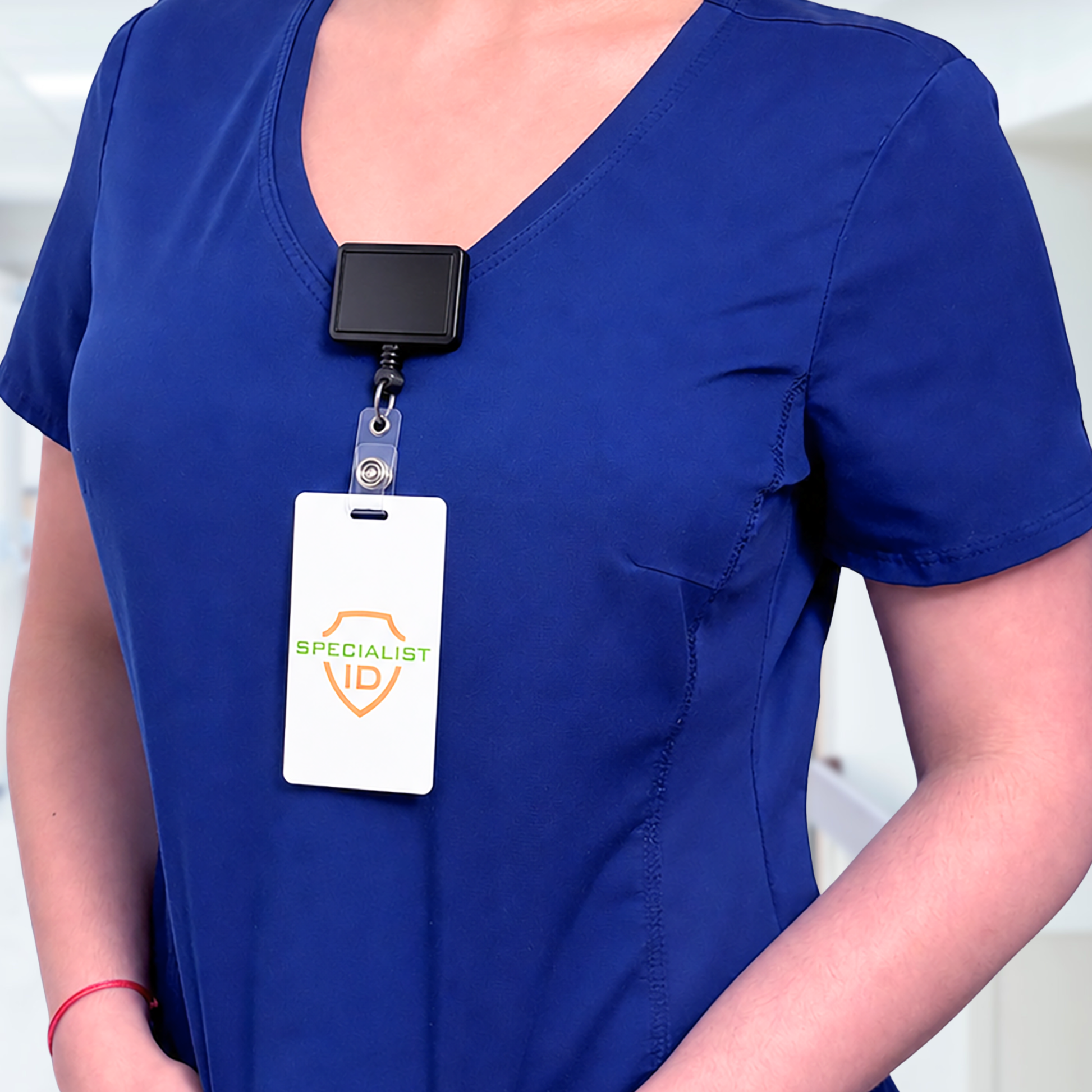 A person in blue medical scrubs wears a Rectangle Badge Reel Retractable with Rotating Swivel Clip (2120-390X), the badge holder clipped to their chest and displaying an ID card labeled "SPECIALIST ID.
