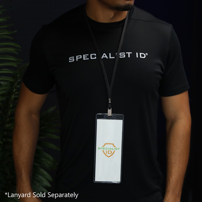A person is wearing a black “Specialist ID” shirt and displaying a pass in the 3X8 Clear Vinyl Vertical Extra Large Badge Holder (506-35875) on a lanyard. This oversized badge holder is perfect for keeping large passes or IDs visible and secure. Text in the corner reads “*Lanyard Sold Separately.”.