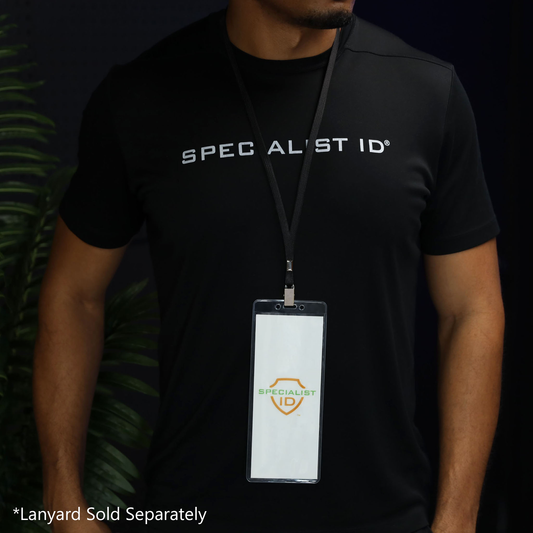 A person is wearing a black “Specialist ID” shirt and displaying a pass in the 3X8 Clear Vinyl Vertical Extra Large Badge Holder (506-35875) on a lanyard. This oversized badge holder is perfect for keeping large passes or IDs visible and secure. Text in the corner reads “*Lanyard Sold Separately.”.