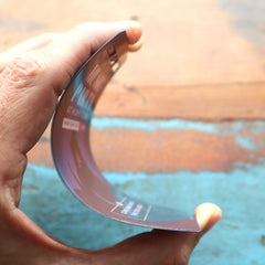 A hand bends a Custom Printed Event Badge with Three Slot Holes—Design It Your Way!—over a wooden surface painted partly blue. Sold by Specialist ID.