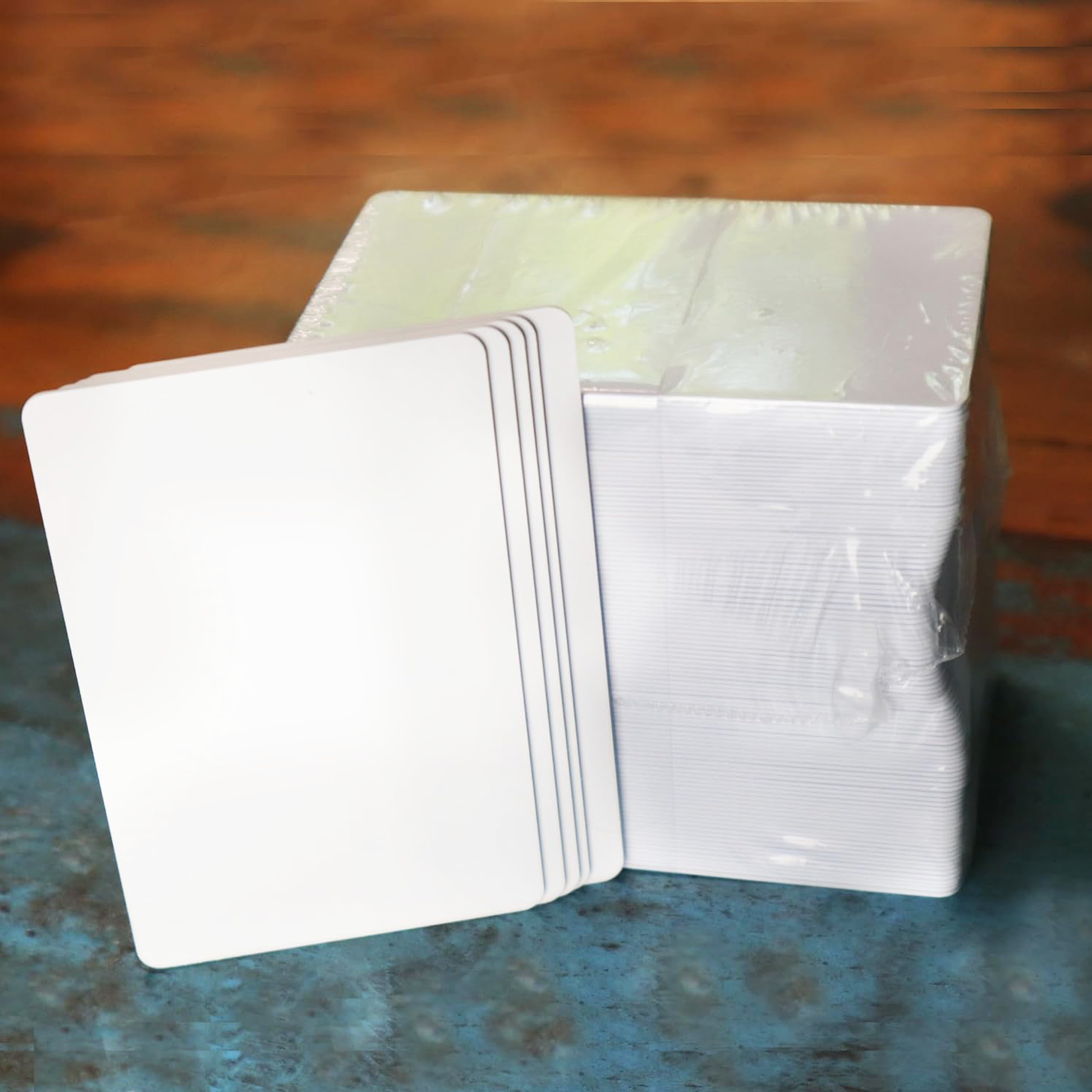 A 500 pack of Professional CR80 30 mil Composite PVC/PET Cards (compatible with most printers), with some cards unwrapped and others still wrapped in plastic, sits on a blue and brown surface.