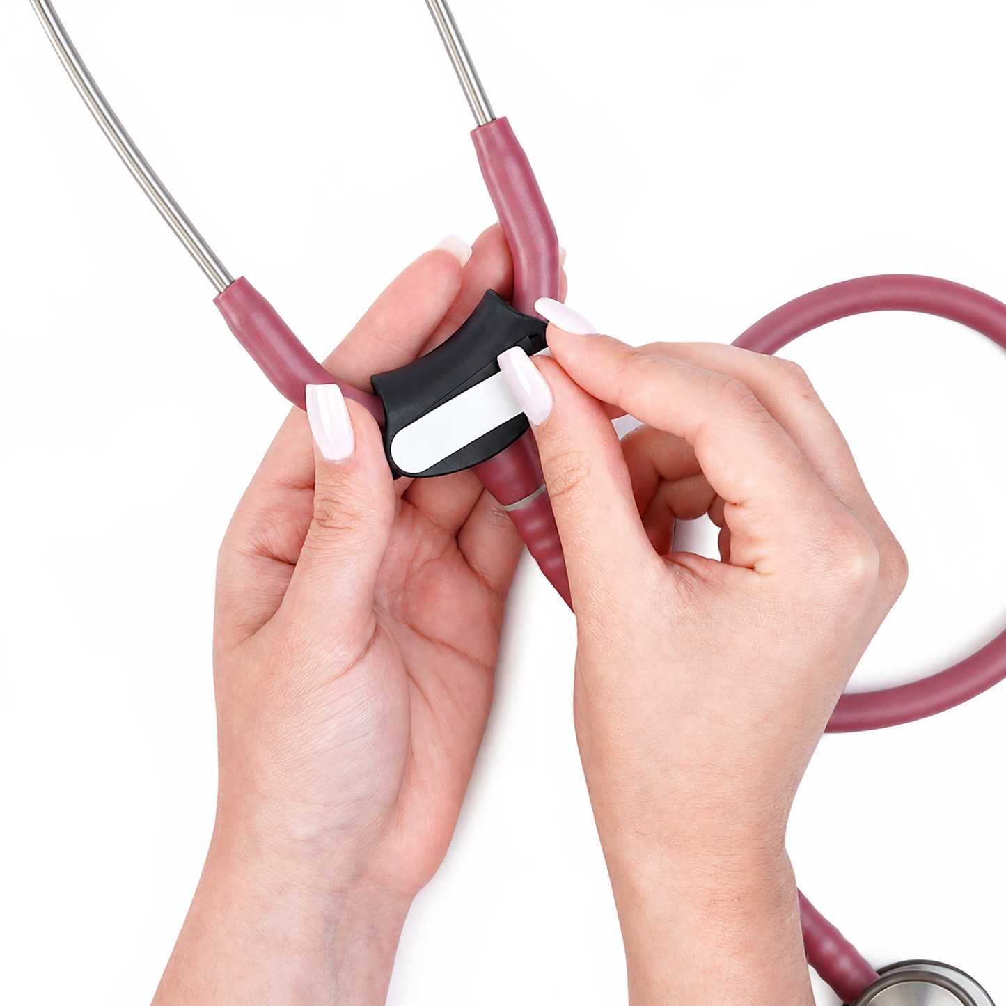 A close-up of a person's hands attaching a white label to the the plastic stethoscope tag of a medical stethoscope with a dusty rose-colored tubing and silver metal chestpiece on a white background.