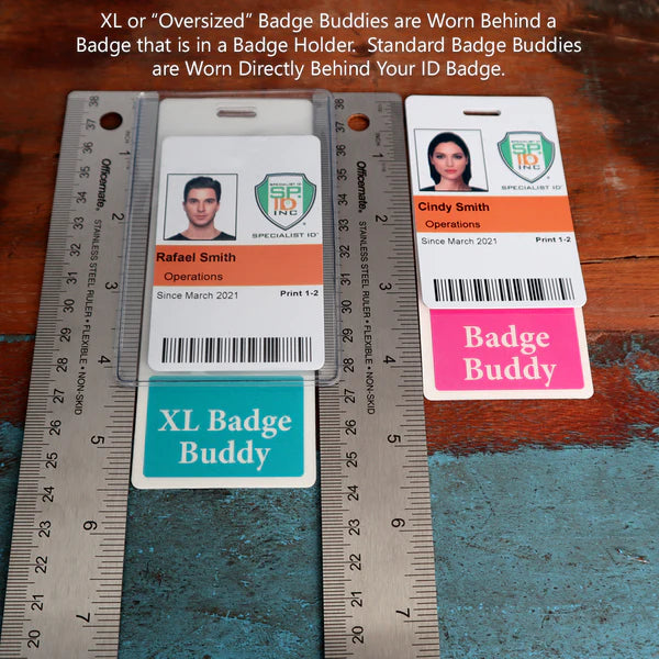 Two employee IDs rest on a wooden surface next to rulers. One, labeled "Rafael Smith," includes a green Fully Customizable Badge Buddy Vertical - (Standard Size) below it. The other, labeled "Cindy Smith," features a pink Fully Customizable Badge Buddy Vertical - (Standard Size). These identification badge holders keep their IDs easily distinguishable and professional.