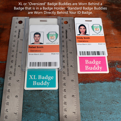 Two ID badges are displayed with attached Badge Buddies—a green "Oversized Fully Customizable Badge Buddy Vertical XL- (Extra Large Size)" for Rafael Smith and a pink "Oversized Fully Customizable Badge Buddy Vertical XL- (Extra Large Size)" for Cindy Smith. Two rulers flank the badges on a wooden table.