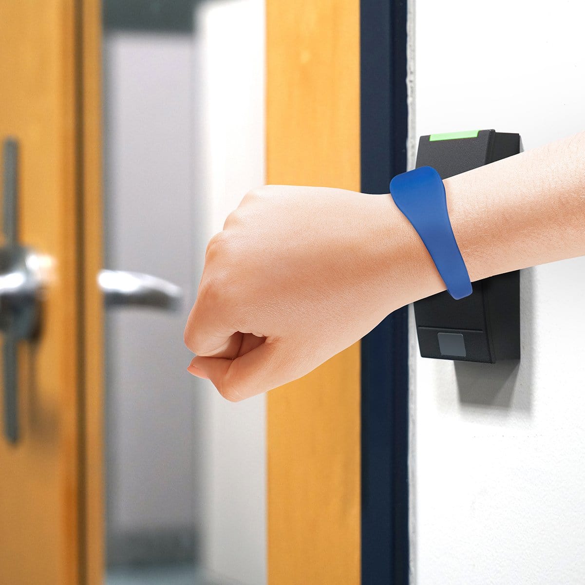 A person wearing a blue silicone U-Band access wristband taps a wall-mounted access control reader beside a door. Sold by Specialist ID.