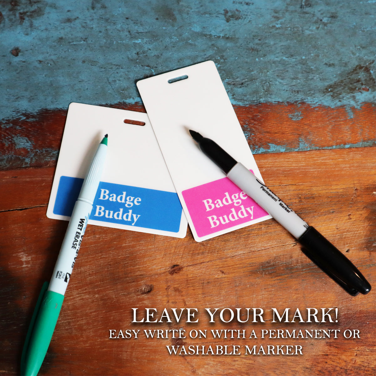 A Nurse Leader Badge Buddy - Vertical Hospital ID Role Identifier with blue and pink labels rests on wood with markers. Text says: "LEAVE YOUR MARK! EASY WRITE ON WITH A PERMANENT OR WASHABLE MARKER.