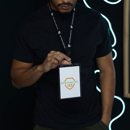 A person in a black shirt holds up a Vertical 4x6 Oversized Vinyl Badge Holder (XL46V) displaying a badge marked “SPECIALIST” with a shield logo, emphasizing the significance of having an event credential holder.
