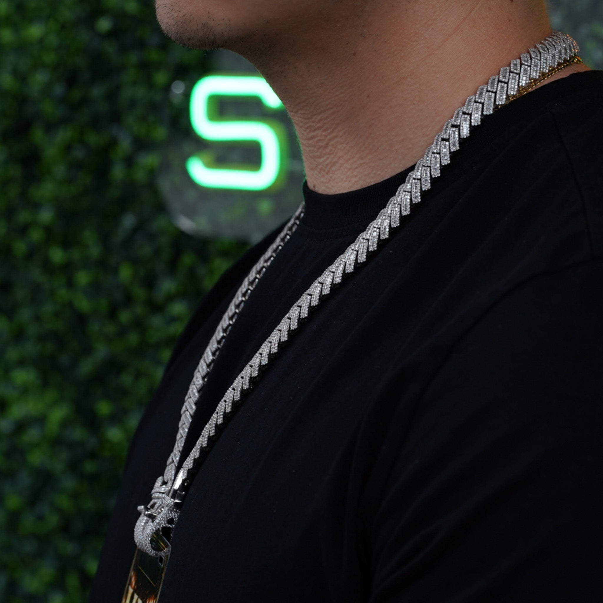 Side profile of model wearing diamond studded VIP credential chain with neon logo background