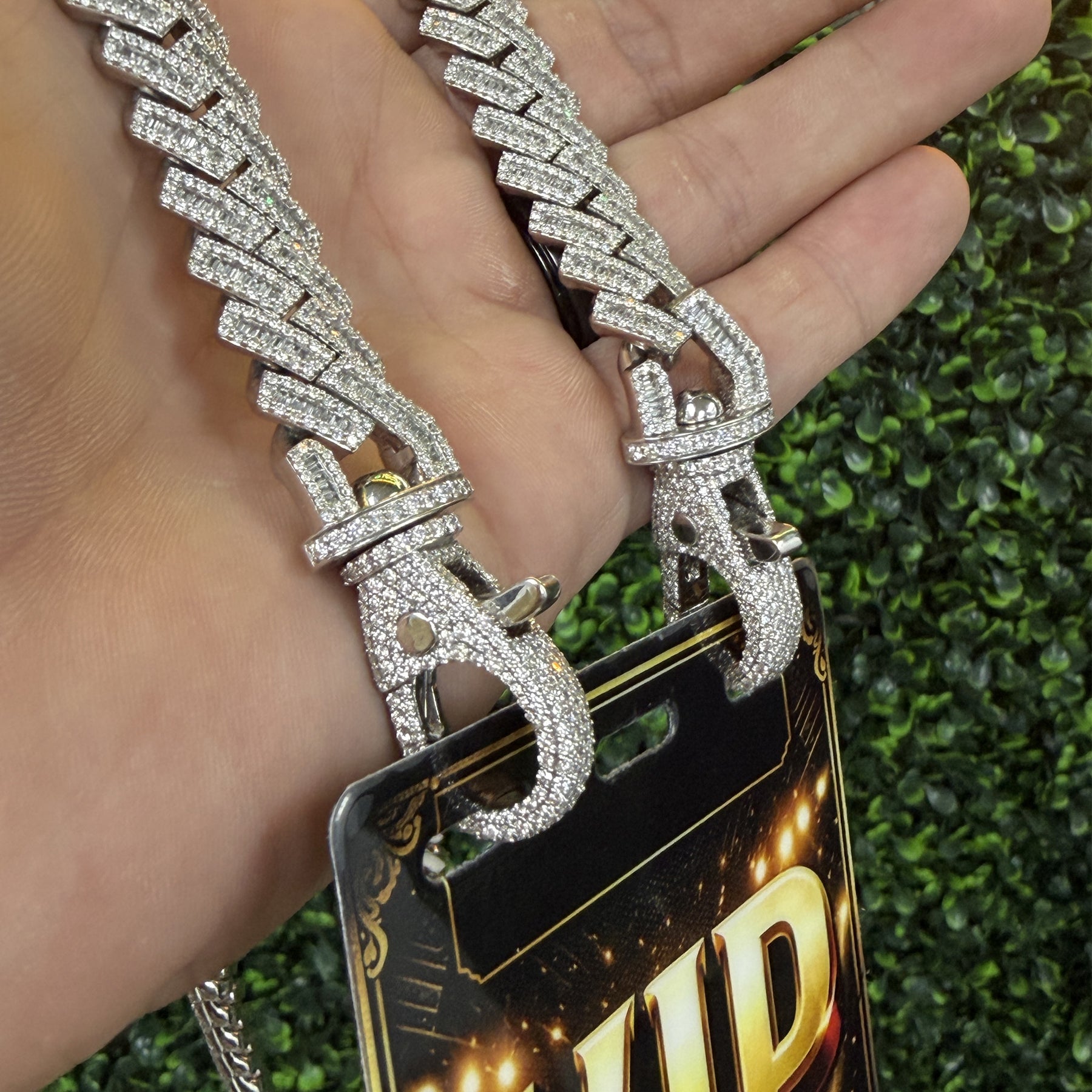 Hand holding diamond studded VIP credential chain with clasps and badge against green background