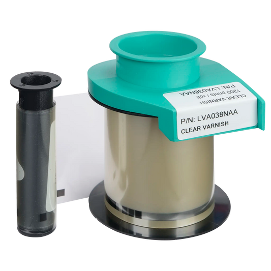 Next to an empty black plastic spool sits the Evolis LVA038NAA Clear Varnish Ribbon, distinguishable by its green and white label. This product, compatible with Primacy2 and Avansia Lamination, provides a protective layer for ID cards and can produce up to 1200 prints, making it ideal for use in ID card printers.