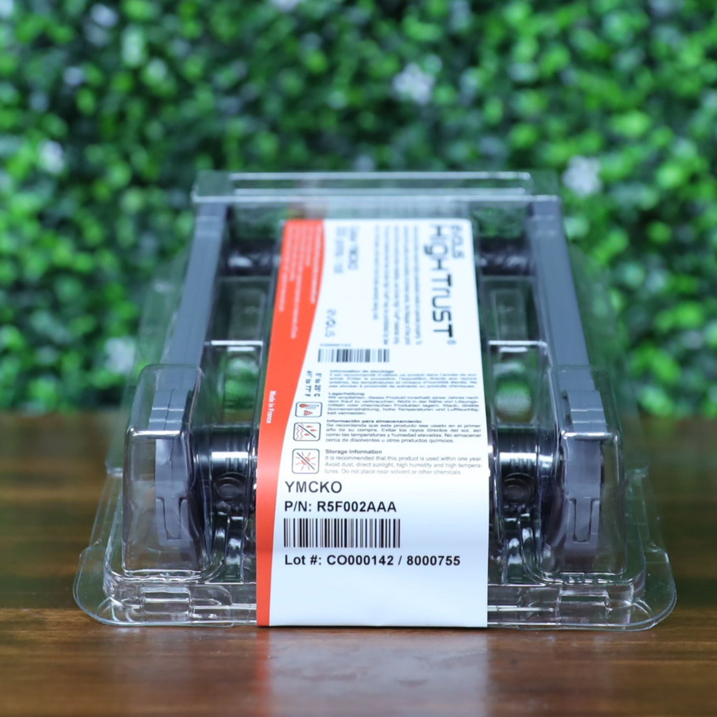 Evolis R5F002AAA YMCKO color ribbon in sealed packaging with visible part number, barcode, and lot number on label. Angled front view on wooden surface. Photographed and sold by Specialist ID, an authorized Evolis dealer.