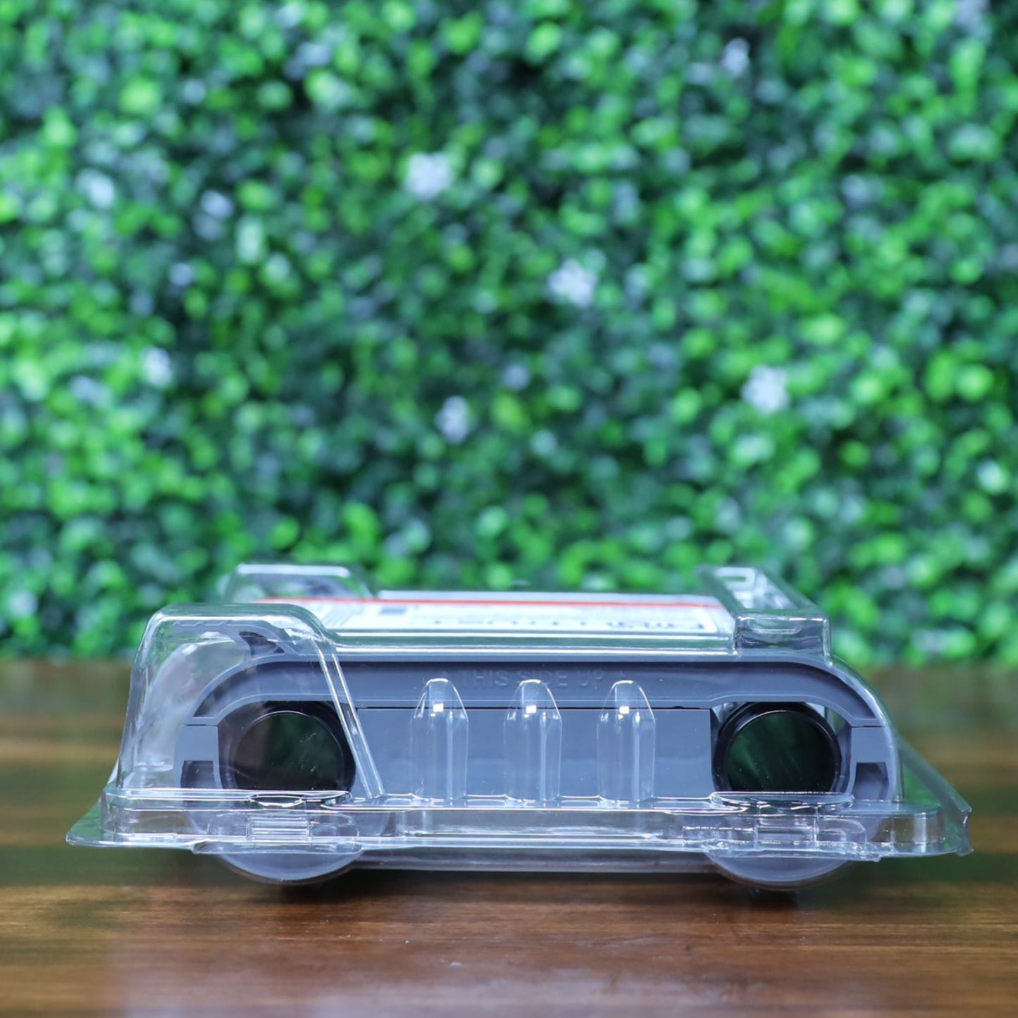 Top-down view of the Evolis R5F002AAA YMCKO ribbon sealed in clear plastic packaging, laying flat on a wooden surface. Ribbon ends and cassette structure visible. Photographed and sold by Specialist ID, an authorized Evolis dealer.