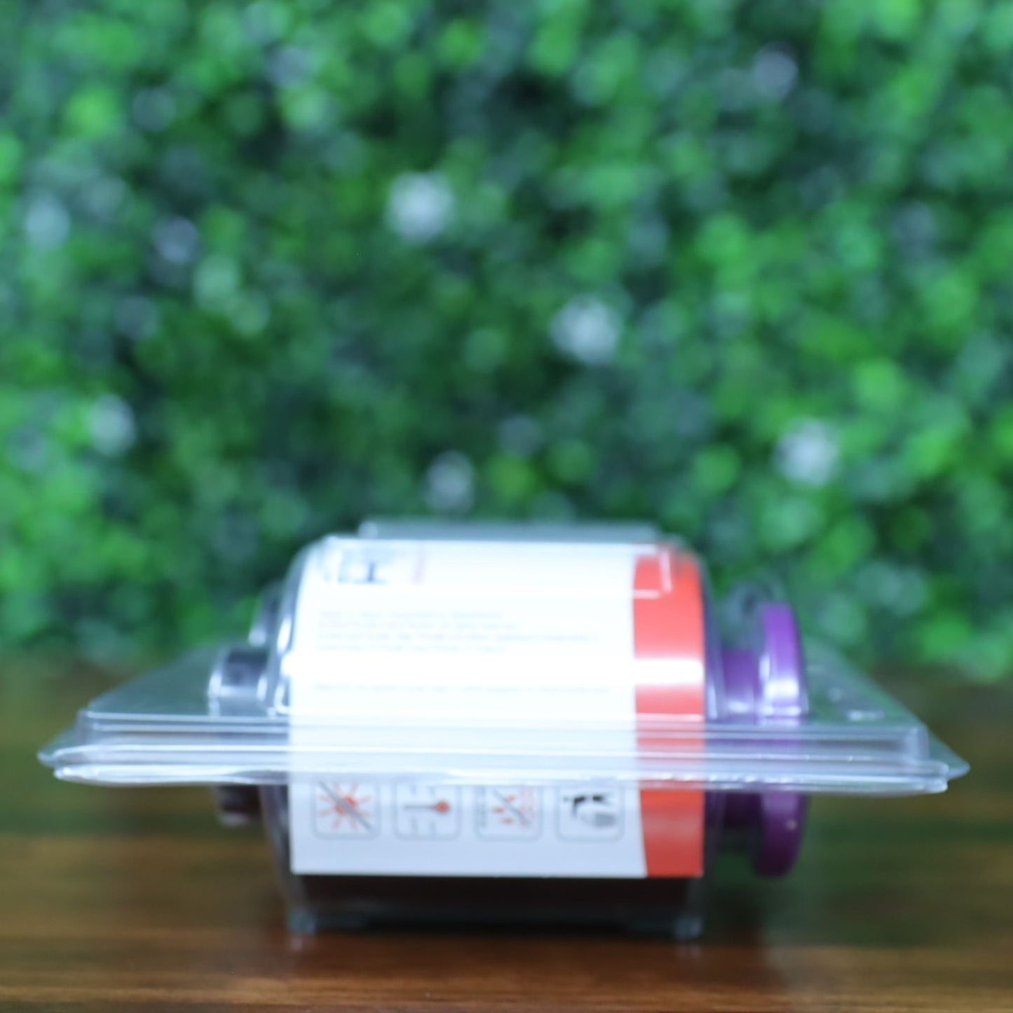 Side profile of Evolis RT4F010AAA YMCK ribbon lying flat in sealed High Trust clamshell packaging, showing purple and black spool ends with safety icons visible. Photographed and sold by Specialist ID, an authorized Evolis dealer.