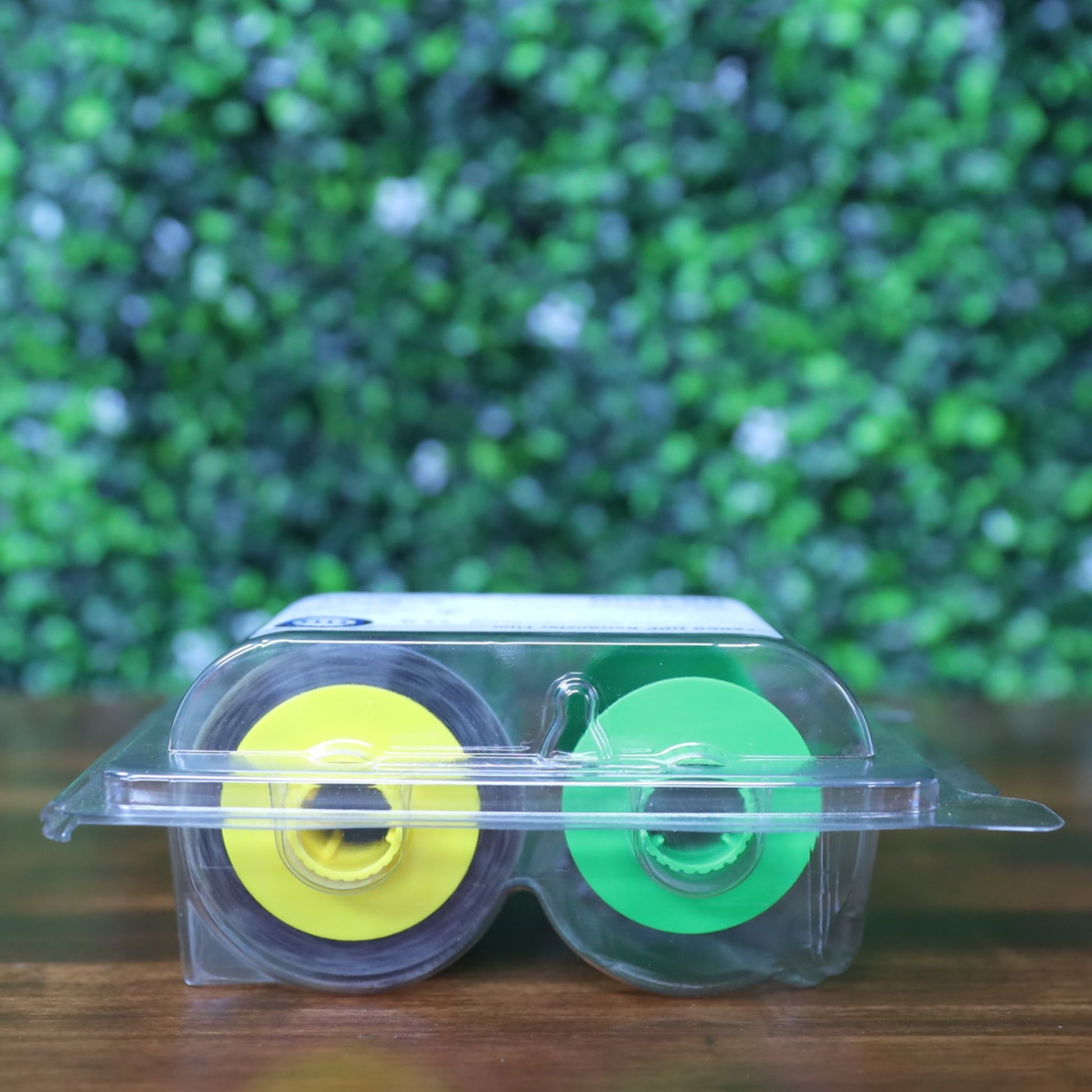 Side view of Fargo 84500 retransfer film in sealed packaging showing yellow and green ribbon spool cores through clamshell case. Photographed and sold by Specialist ID, an authorized HID Fargo dealer.