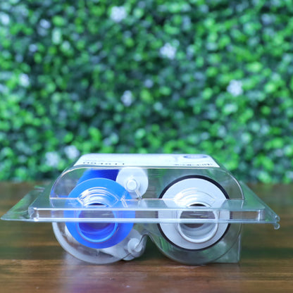 Top view of HID Fargo 84811 YMCK color ribbon showing blue and white spool cores through clear clamshell packaging, lying flat against a wood surface with blurred green backdrop. Photographed and sold by Specialist ID, an authorized HID Fargo dealer.