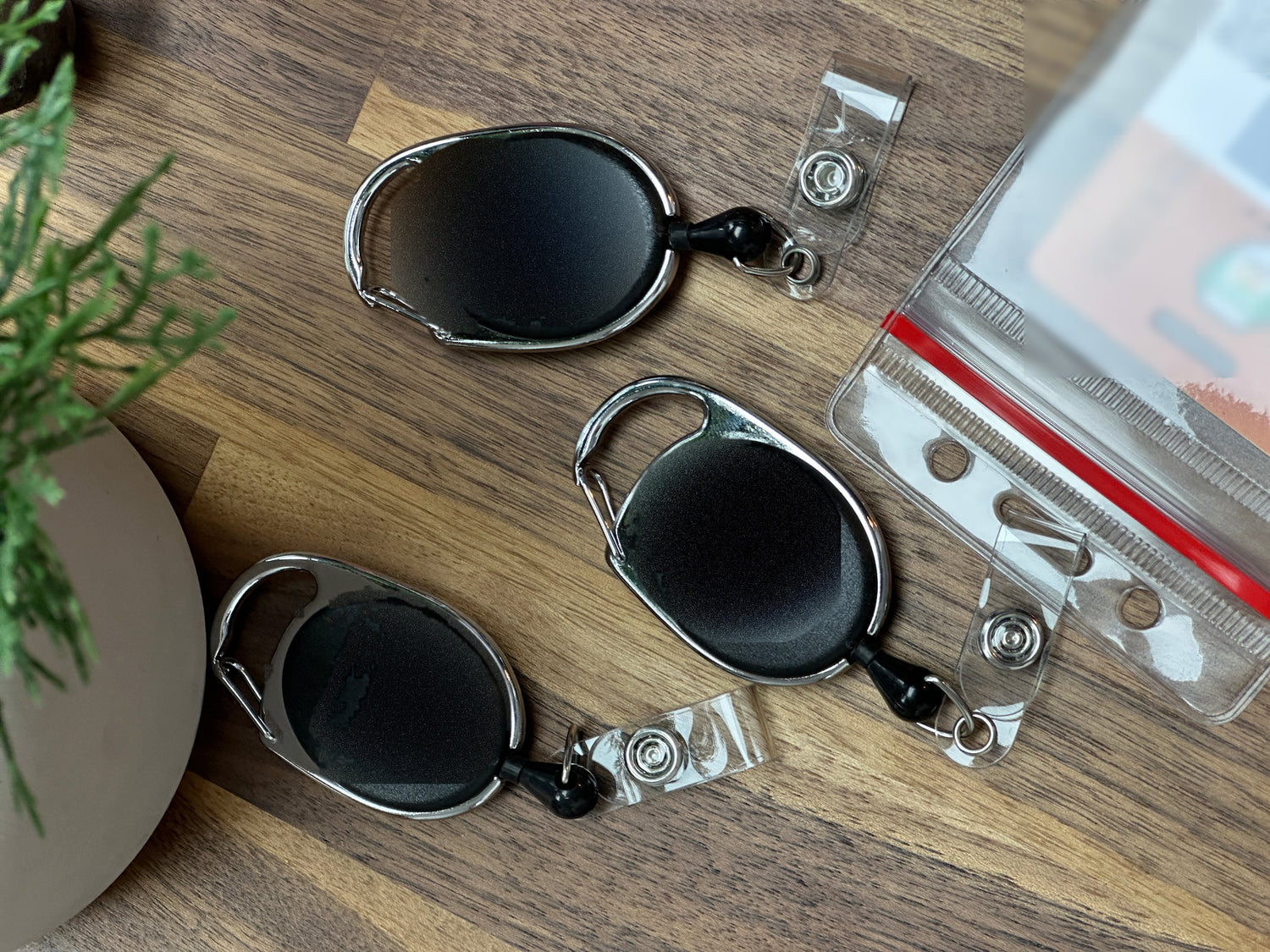 Three SpecialistID carabiner badge reels and a clear badge holder on a wooden desk