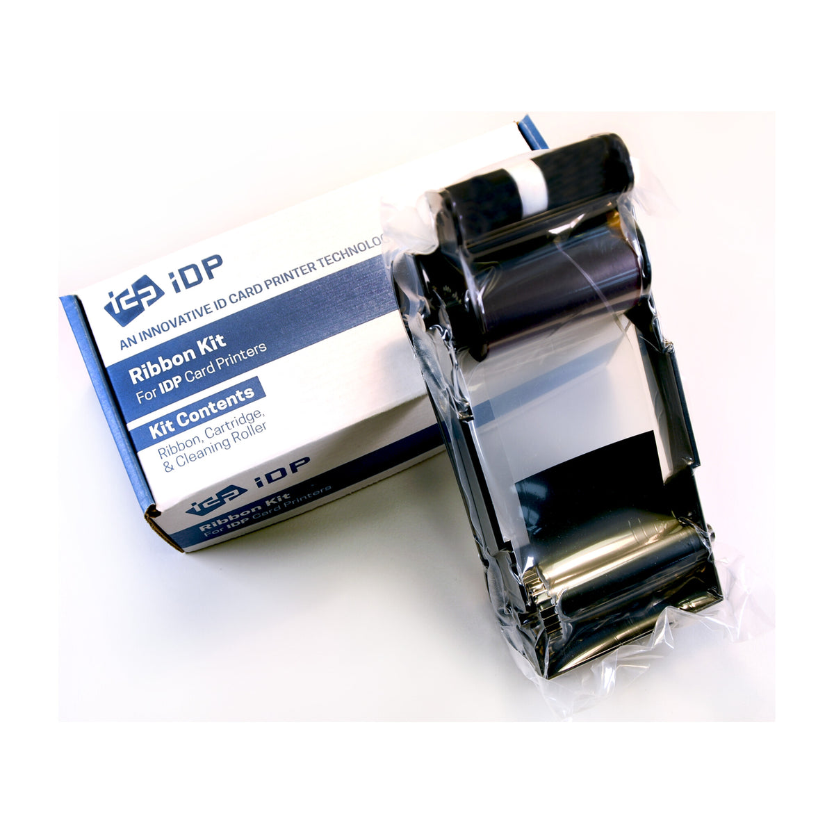 IDP 900900 ribbon kit: ribbon cassette in its wrapper resting on the IDP Ribbon Kit box, which lists ribbon, cartridge and cleaning roller