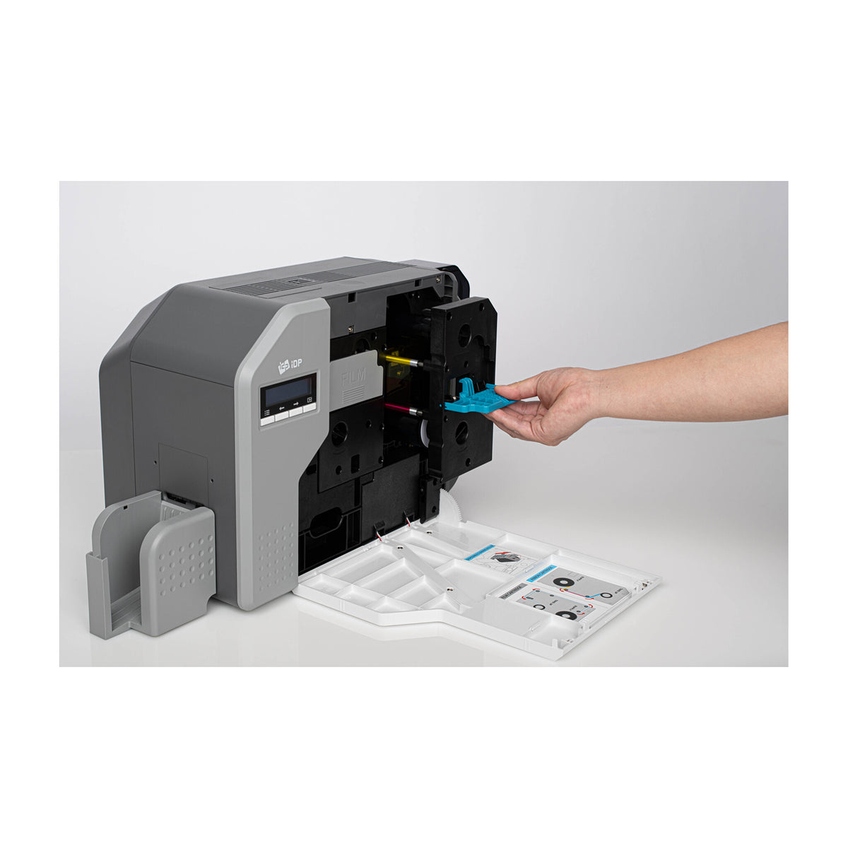 SMART-81HD with its front cover folded down, showing the ribbon and retransfer film cartridges while a hand fits the blue disposable cleaning roller